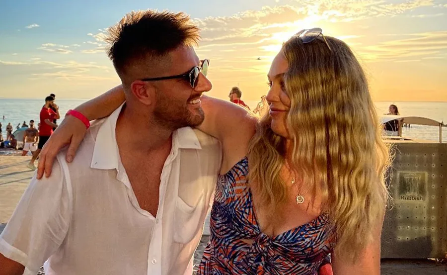 Couple smiling at each other during sunset on a beach with the ocean in the background.