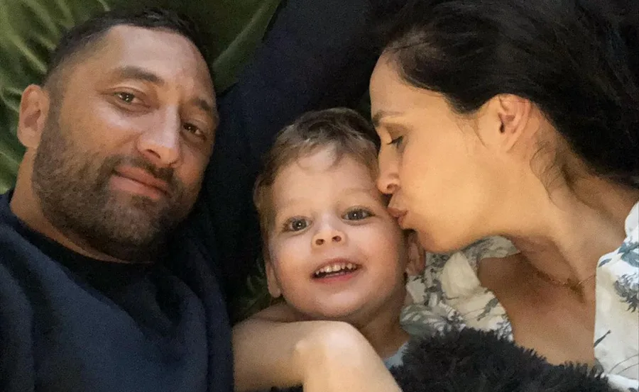 Family selfie with a man smiling, a woman kissing a child's cheek, and the child smiling at the camera.