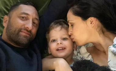 Family selfie with a man smiling, a woman kissing a child's cheek, and the child smiling at the camera.