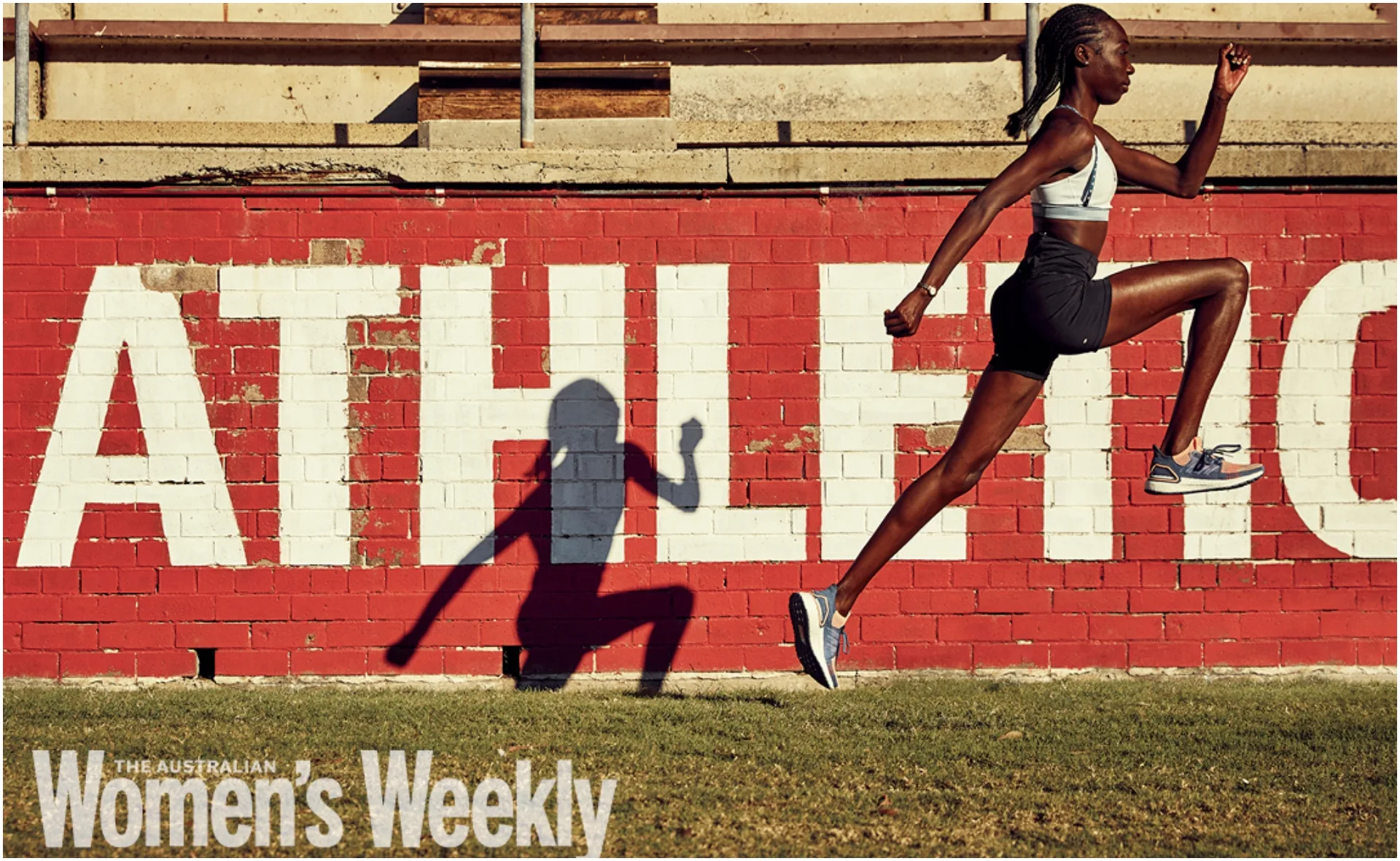 Female athlete in mid-air leap, casting a shadow on a red and white wall with "ATHLETICS."