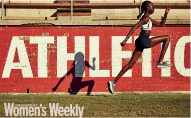 Female athlete in mid-air leap, casting a shadow on a red and white wall with "ATHLETICS."