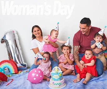 Family with quadruplets celebrates first birthday with colorful decorations and cake.