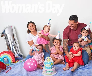 Family with quadruplets celebrates first birthday with colorful decorations and cake.