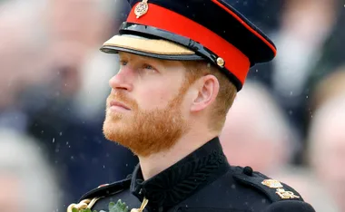 A man in a formal military uniform and hat looks upwards, with a blurred crowd in the background.