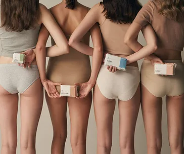Four women in underwear holding various Lovekins sanitary pad packages behind their backs.