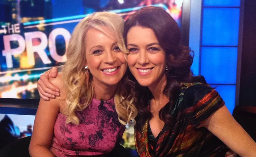 Two women smiling and embracing each other on a TV show set with the word "PRO" visible in the background.