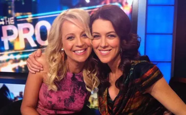 Two women smiling and embracing each other on a TV show set with the word "PRO" visible in the background.