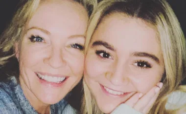 Two smiling women in a close-up selfie, showing a friendly and happy moment.