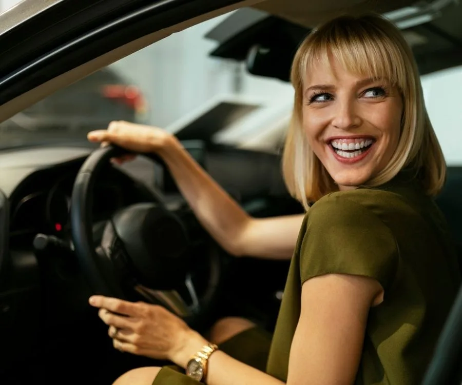 Woman smiling while sitting in the driver's seat of an SUV, looking back over her shoulder.