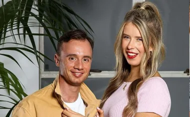 Man and woman smiling indoors, with plants in the background.