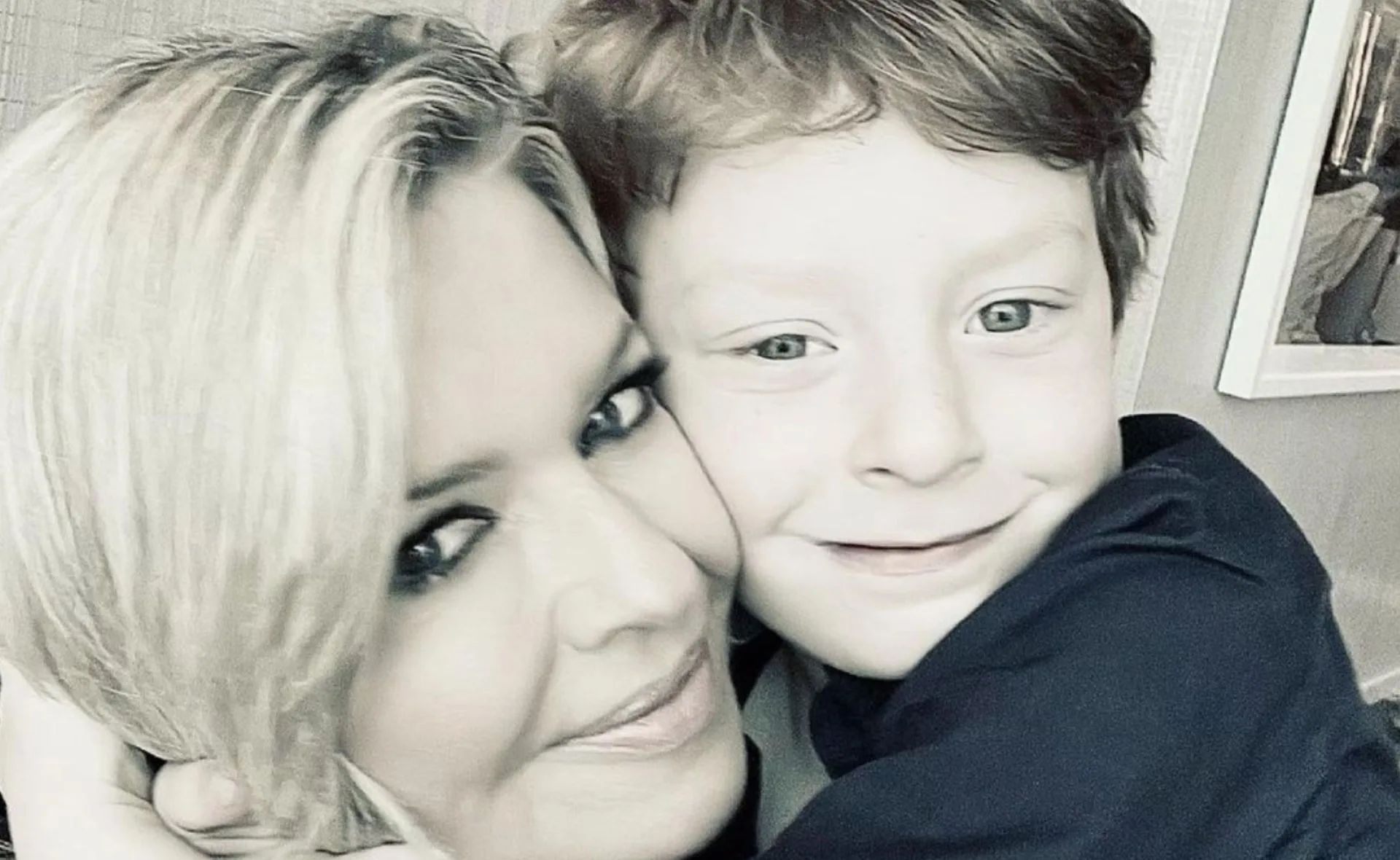 A woman with short blonde hair and a young boy with light hair, smiling and hugging in a close-up photo.