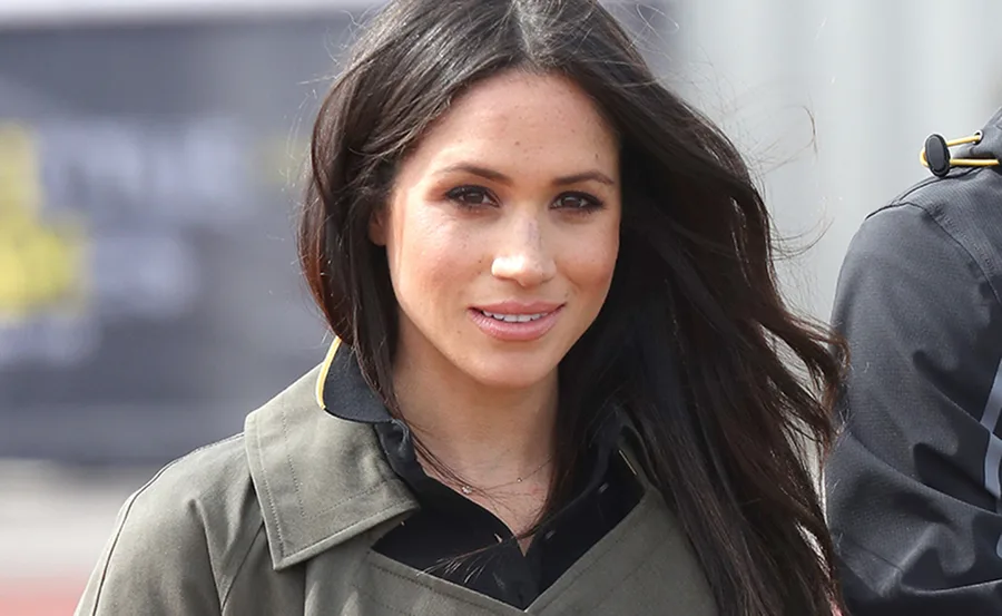 Young woman with long dark hair, wearing a gray jacket outdoors, smiling at the camera.