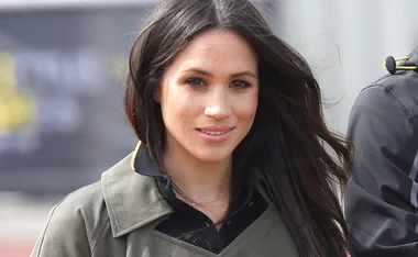 Young woman with long dark hair, wearing a gray jacket outdoors, smiling at the camera.
