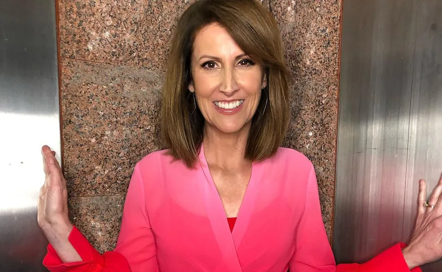 Smiling woman in a pink ombre blouse stands against a textured wall.
