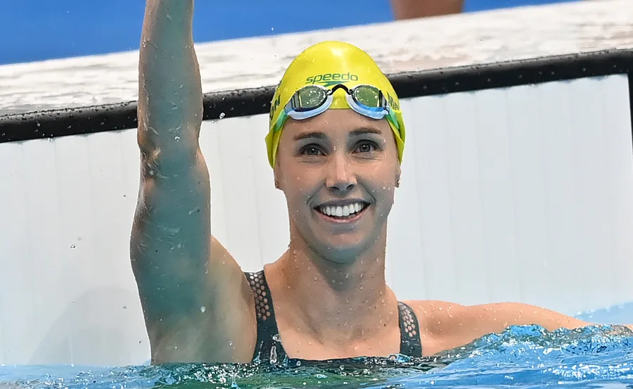 Swimmer wearing a yellow cap, smiling and raising one arm in a pool.