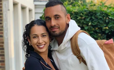 A smiling couple poses closely outdoors, with greenery in the background.