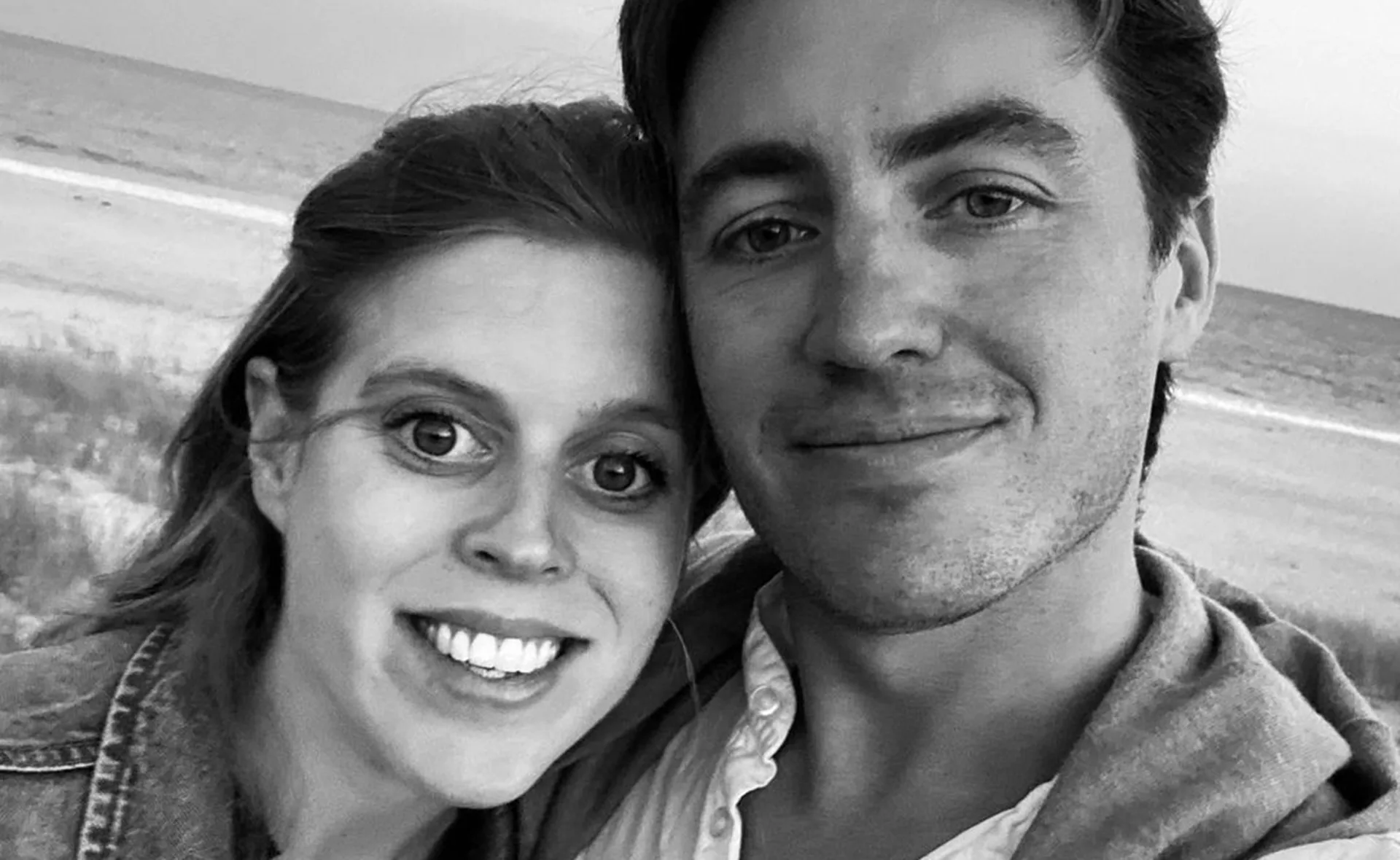 A woman and man smiling on a beach, with the ocean in the background, black and white image.