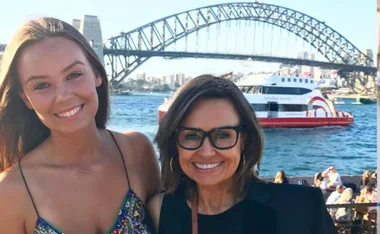 Two people smiling with the Sydney Harbour Bridge in the background, near the water, on a sunny day.