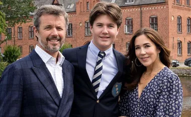 Family posing together in front of a brick building, with the young man in a school uniform.