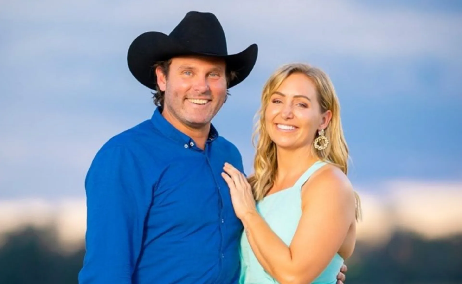 Man in a cowboy hat with a woman in a light blue dress smiling outdoors.