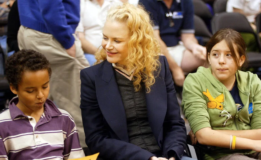 A woman with curly hair sitting between two children at an event.