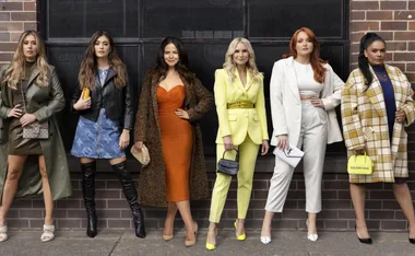 Women in diverse stylish outfits pose confidently against a wall, showcasing fashion trends.