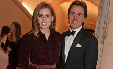 Couple posing elegantly at an event, with a warmly lit background.