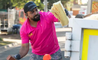 Construction worker in pink shirt labeled "RONNIE" placing insulation material into a container outdoors.