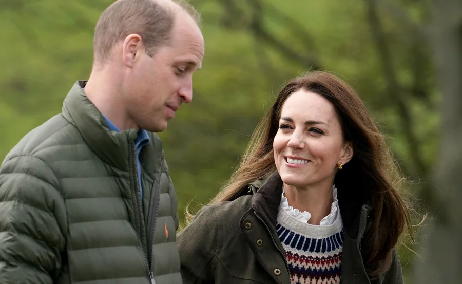 A man and woman walking outdoors, smiling and engaged in conversation against a green blurred background.
