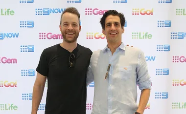 Two men smiling in front of a white background with logos for Nine Network channels like Gem and Life.