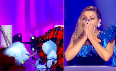 A performer in a blue monster costume is revealed on stage, while a judge reacts surprised, covering her mouth.