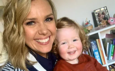 Smiling woman and toddler taking a selfie in a room with books and photos in the background.