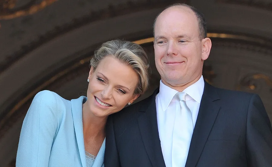 A couple smiling, the woman in a light blue outfit leaning on the man's shoulder, both looking content.