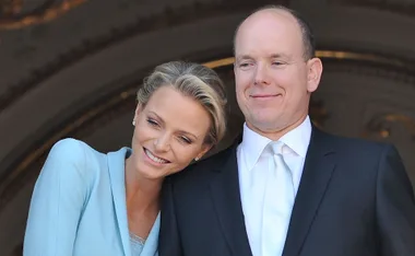 A couple smiling, the woman in a light blue outfit leaning on the man's shoulder, both looking content.