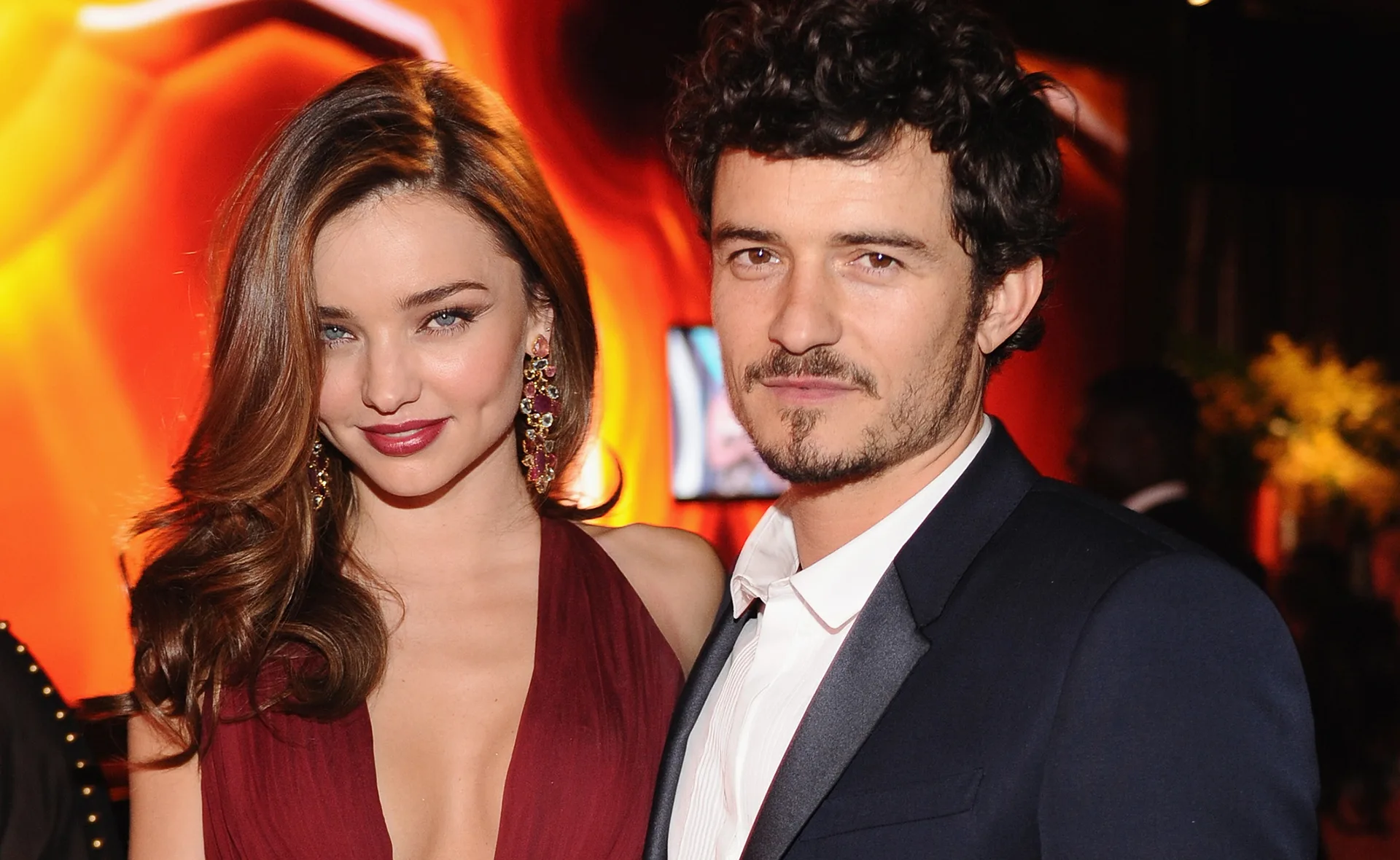 A couple posing together at a formal event with warm, elegant lighting in the background.