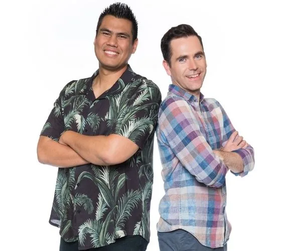 Two men smiling confidently with arms crossed, one in a tropical shirt and the other in a plaid shirt, on a white background.