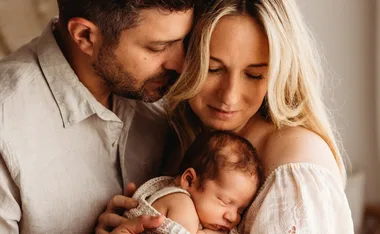 A couple lovingly holds a newborn baby close, cherishing the moment together.
