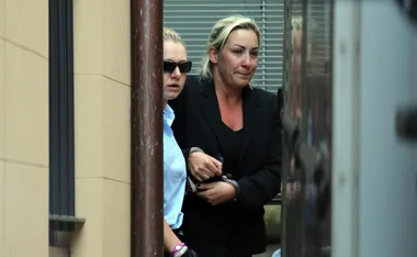 Two women, one wearing sunglasses, walking outdoors near a building; one appears in custody.