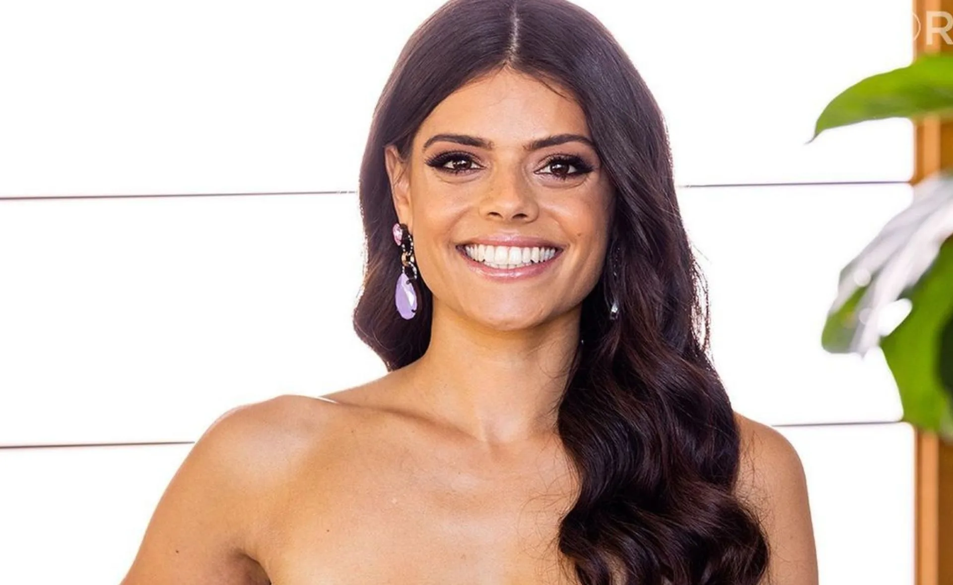 Smiling woman with long hair and dangling earrings in a bright setting.