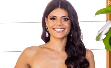 Smiling woman with long hair and dangling earrings in a bright setting.