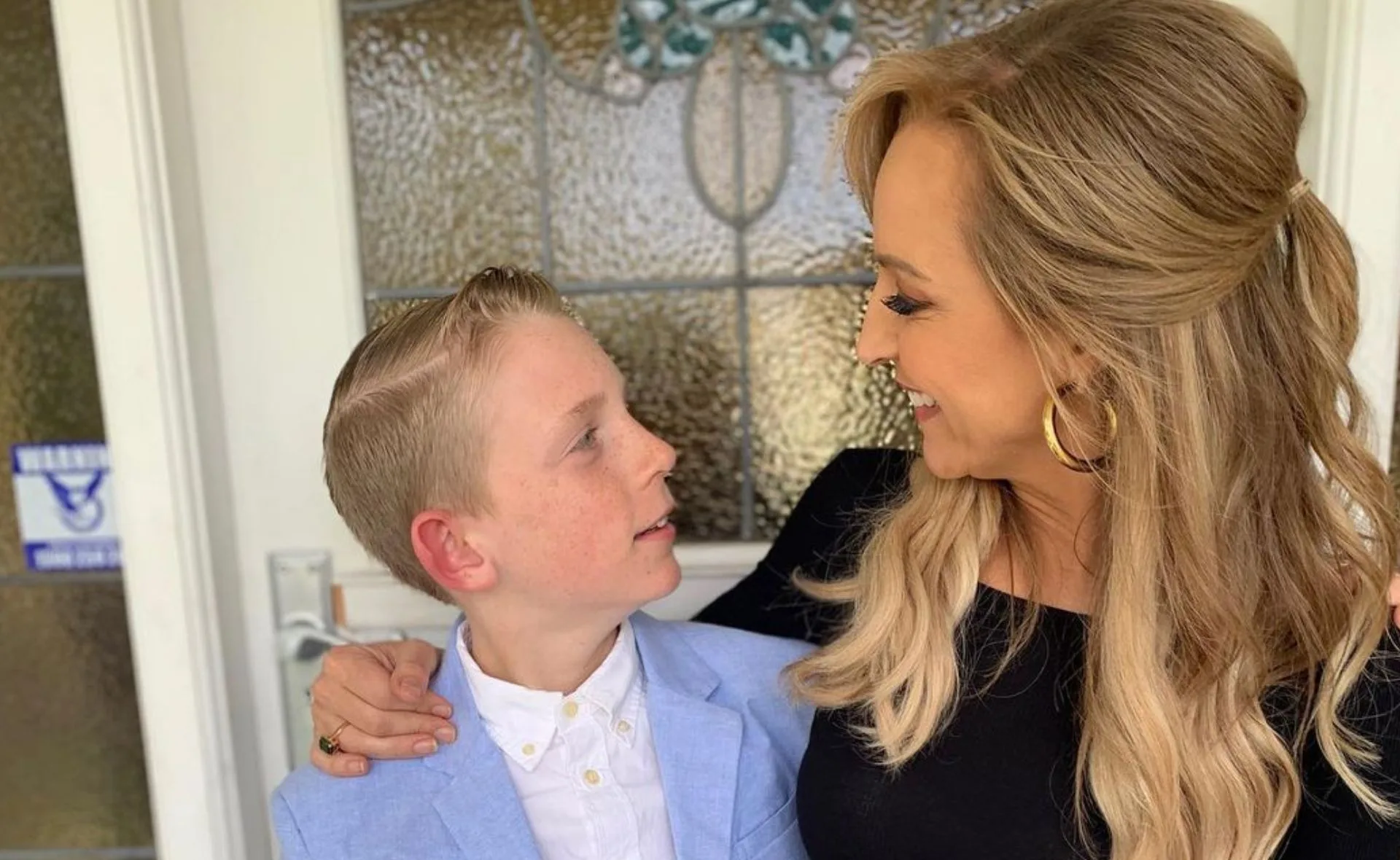 Woman and young boy smiling at each other in front of a glass door.