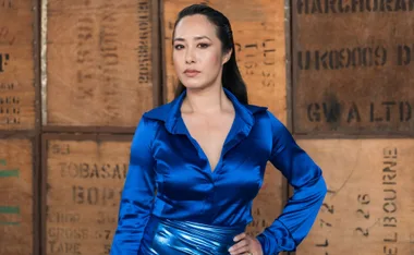 A person in a blue shirt poses confidently with a hand on hip, against a wooden box backdrop.