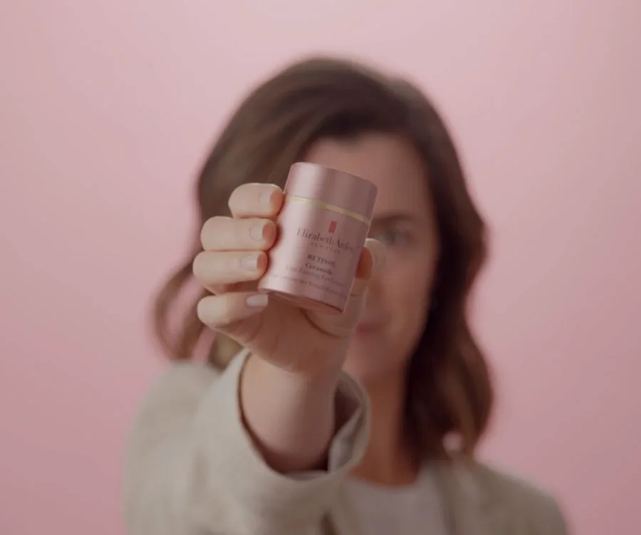 Elizabeth Arden ceramide eye cream held by a woman against a soft pink background.