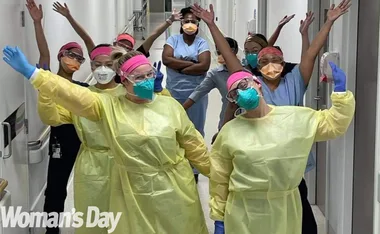Nurses in protective gear celebrate in a hospital corridor, expressing gratitude and positivity during COVID-19.