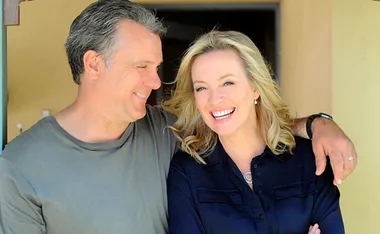 A smiling man and woman standing close together outdoors, with his arm around her shoulder.