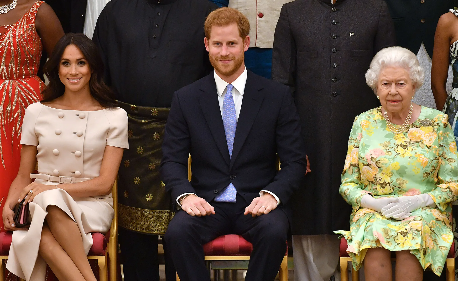 A seated group photo with individuals in formal attire, including a woman in a cream dress and a man in a suit.