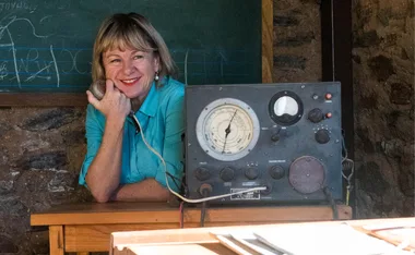 Woman with headset at retro radio console, smiling in classroom setting.