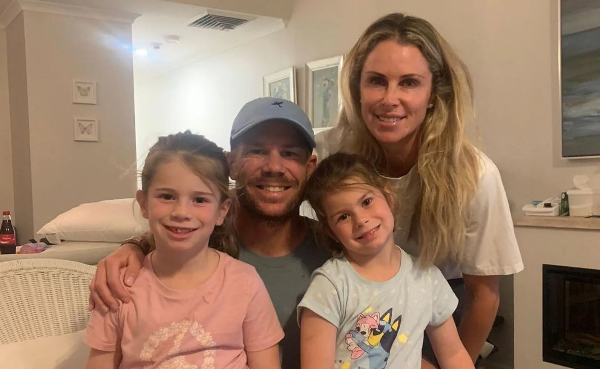 A family of four posing for a photo, two adults and two young children smiling indoors.