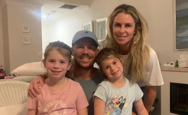 A family of four posing for a photo, two adults and two young children smiling indoors.