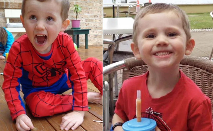 Young boy in a Spider-Man suit laughing and smiling at an outdoor setting.